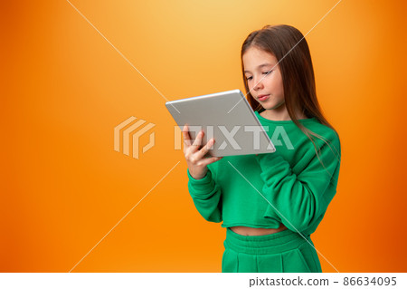 Beautiful teen girl using digital tablet over orange studio background 86634095