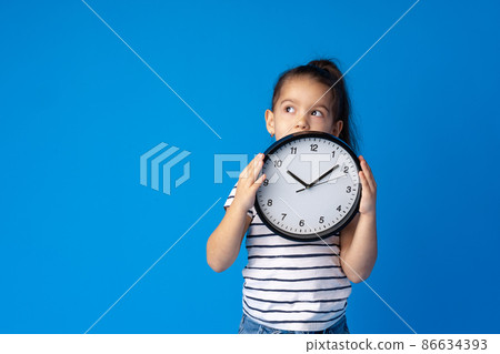 Beautiful teen girl holding wall clock over blue background 86634393