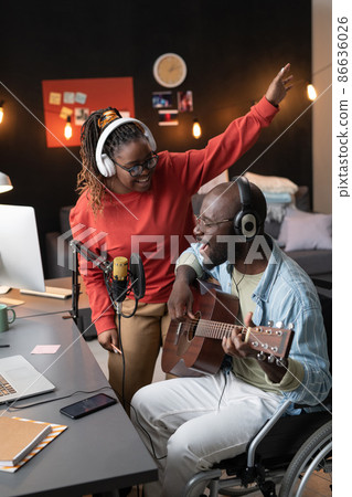 Happy African man with disability playing guitar and singing a song together with woman during live broadcasting Happy African man with disability playing guitar and singing a song together with woman during live broadcasting 86636026