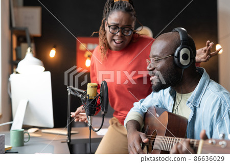 African young woman singing a song while man in headphones playing guitar, they performing during live broadcasting African young woman singing a song while man in headphones playing guitar, they performing during live broadcasting 86636029