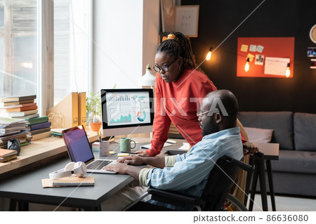 African man with disability working on laptop at the table together with his colleague during their work at home 86636080