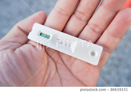Human hand displays a Covid-19 positive result cassette from a rapid antigen test kit (ATK) 86639331