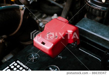Battery anode terminal with red plastic cover is installed on a black battery in a electric system Battery anode terminal with red plastic cover is installed on a black battery in a electric system 86639347