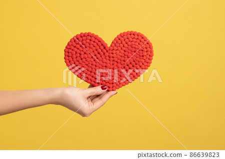Profile side view closeup of woman hand holding red heart, showing romantic feelings. Indoor studio shot isolated on yellow background. 86639823
