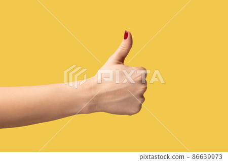 Profile side view closeup of woman hand showing like or thumbs up, approved, positive feedback. Indoor studio shot isolated on yellow background. Profile side view closeup of woman hand showing like or thumbs up, approved, positive feedback. Indoor studio shot isolated on yellow background. 86639973