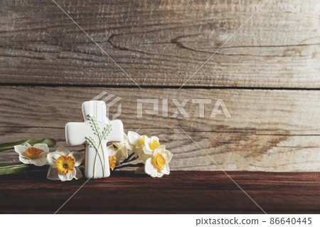 Easter holiday conceptual background on rustic wooden boards. Photo of gingerbread cookie Cross shape, narcissus or daffodils flowers on table top. Card with copy space to place text. Minimal concept Easter holiday conceptual background on rustic wooden boards. Photo of gingerbread cookie Cross shape, narcissus or daffodils flowers on table top. Card with copy space to place text. Minimal concept 86640445