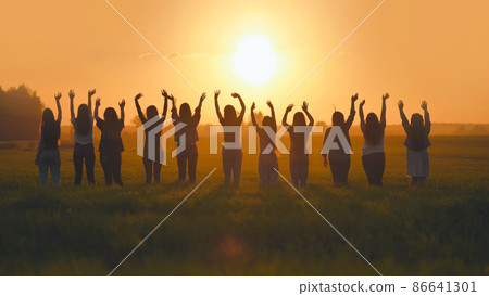 Silhouette of friends of 11 girls waving their hands at sunset in the field. 86641301