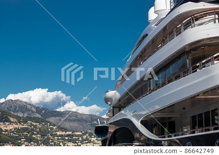 The top deck of a huge yacht at sunny day, glossy board of the boat, The chrome plated handrail, megayacht is moored in port, sun reflection on glossy board, mountain on background 86642749