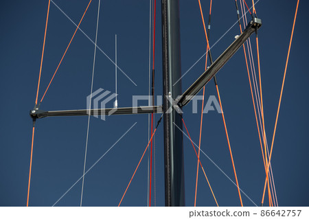 Close up view of the mast of huge sailboat at clear weather, blue sky on a background, ropes by red color 86642757