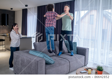 Man with boy jumping on couch and surprised woman 86642852