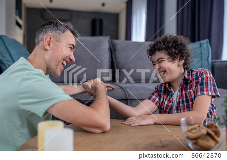 Cheerful man and boy competing in arm wrestling 86642870