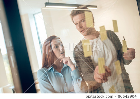 Man and woman looking at notes on wall debating 86642904