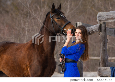A beautiful girl with a horse is standing near an old wooden fence A beautiful girl with a horse is standing near an old wooden fence 86643072