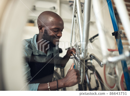 Bikes are my passion. Shot of a handsome young man crouching in his shop and repairing a bicycle wheel. Bikes are my passion. Shot of a handsome young man crouching in his shop and repairing a bicycle wheel. 86643731