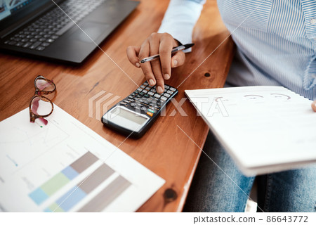 Business is a numbers game. Cropped shot of a businesswoman using a calculator while going over financial paperwork at her desk. Business is a numbers game. Cropped shot of a businesswoman using a calculator while going over financial paperwork at her desk. 86643772
