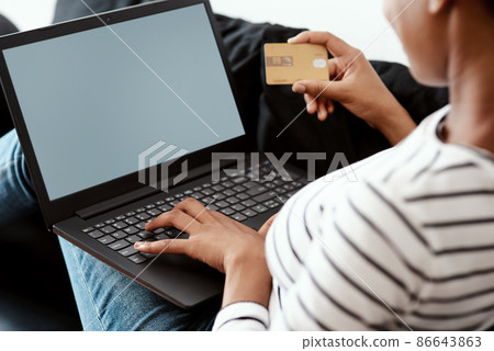 Timeout in the cyberspace shopping mall. Cropped shot of a woman using a laptop and credit card on the sofa at home. Timeout in the cyberspace shopping mall. Cropped shot of a woman using a laptop and credit card on the sofa at home. 86643863