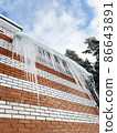 Huge icicles on the edge of the roof of a brick cottage. Heat loss in cold snowy winter. 86643891