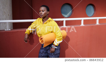 A breath is a beautiful refusal to become anything less. Shot of a young woman holding an exercise mat looking thoughtful against an urban background. 86643912