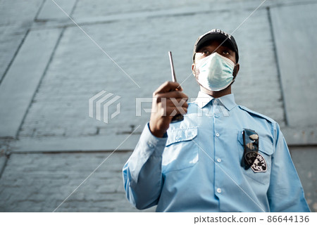 Proactive guarding for your propertys protection. Shot of a masked young security guard using a two way radio while on patrol outdoors. Proactive guarding for your propertys protection. Shot of a masked young security guard using a two way radio while on patrol outdoors. 86644136