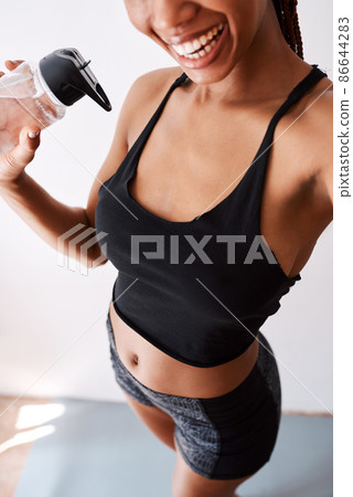 Hitting the gym feels good. Selfie view of a woman holding her water bottle while posing in her gym clothes. Hitting the gym feels good. Selfie view of a woman holding her water bottle while posing in her gym clothes. 86644283