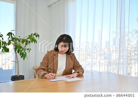 A woman writing an address on an airmail envelope at the desk in the room 86644801