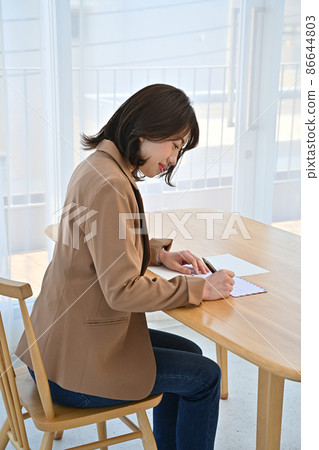 一位女士在房間辦公桌上的航空信封上寫地址 86644803