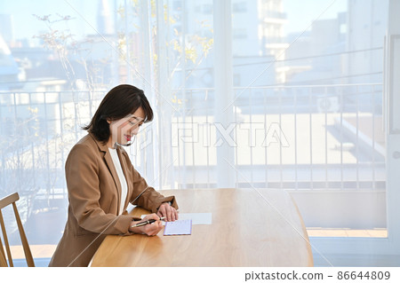 一位女士在房間辦公桌上的航空信封上寫地址 86644809