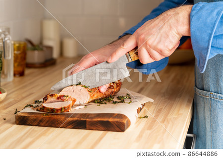 Unrecognizable man cuting with large knife baked pork tenderloin on cutting board Unrecognizable man cuting with large knife baked pork tenderloin on cutting board 86644886