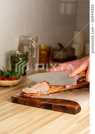 Unrecognizable man cuting with large knife baked pork tenderloin on cutting board, vertical Unrecognizable man cuting with large knife baked pork tenderloin on cutting board, vertical 86644888