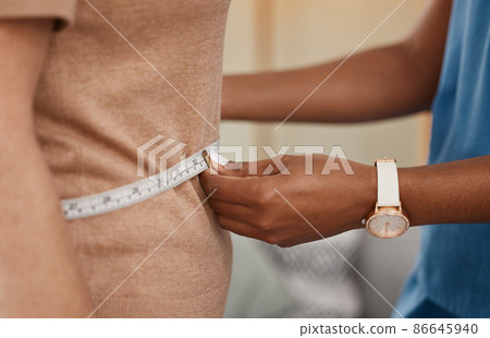 Just the weight its supposed to be. Shot of a doctor using a measuring tape on a senior womans stomach during a consultation at home. 86645940