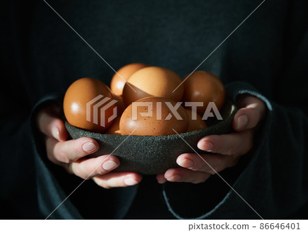 Unusual Easter on dark background. Bowl of brown eggs with hands. Unusual Easter on dark background. Bowl of brown eggs with hands. 86646401