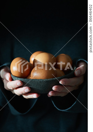 Unusual Easter on dark background. Bowl of brown eggs with hands, vertical Unusual Easter on dark background. Bowl of brown eggs with hands, vertical 86646402