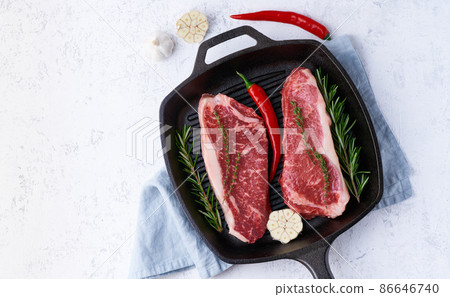 Two fresh raw pieces of meat, beef fillet, marble striploin in cast-iron large pan. Top view Two fresh raw pieces of meat, beef fillet, marble striploin in cast-iron large pan. Top view 86646740