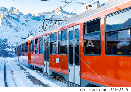 Red train running on rack railway through snowy Swiss Alps 86648749