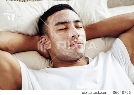 Take a some time out for yourself, you deserve it. Shot of a man wearing a cosmetic face mask while lying on his bed at home. Take a some time out for yourself, you deserve it. Shot of a man wearing a cosmetic face mask while lying on his bed at home. 86648796