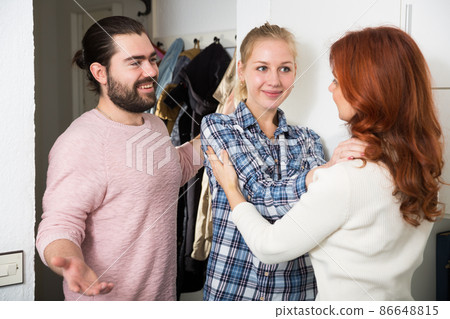 Mother and adult children standing near door and hugging at home Mother and adult children standing near door and hugging at home 86648815