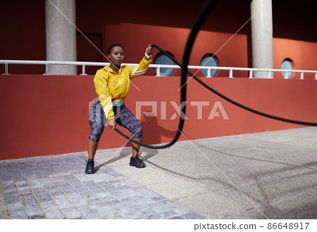 Turning pain into power. Shot of a young woman using battle ropes against an urban background. Turning pain into power. Shot of a young woman using battle ropes against an urban background. 86648917