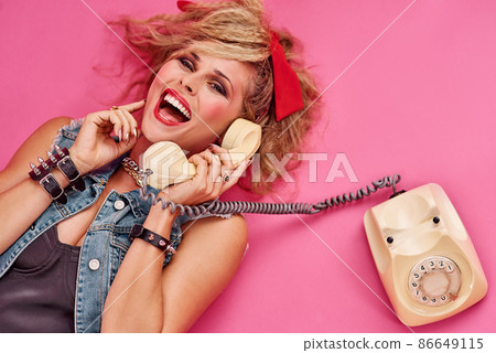 Everyone had so much fun in the 80s. Studio shot of a young woman holding a telephone while wearing 80s clothing. 86649115