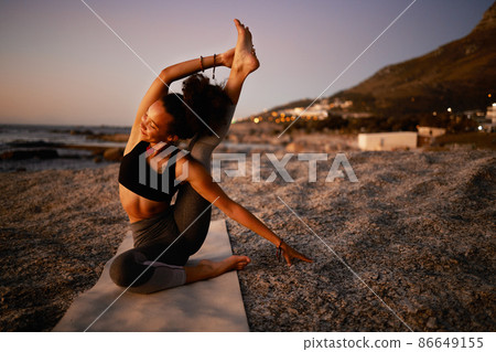 Yoga can heal your soul. Full length shot of an attractive young woman practicing yoga on the beach at sunset. 86649155