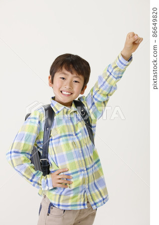 A boy carrying a school bag on his back and raising one hand A boy carrying a school bag on his back and raising one hand 86649820