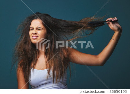 Nip, snip, girl, get a grip. Studio shot of a beautiful young woman pulling on her hair posing against a blue background. 86650193