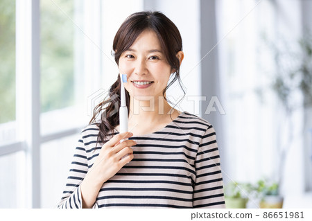 A woman trying to brush her teeth with an electric toothbrush 86651981