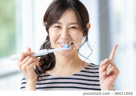 A woman trying to brush her teeth with an electric toothbrush 86651988