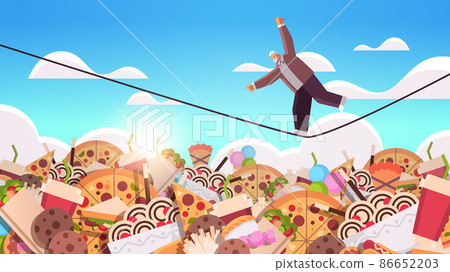 senior man balancing on rope above junk food assortment of fast food unhealthy nutrition junkfood addiction concept senior man balancing on rope above junk food assortment of fast food unhealthy nutrition junkfood addiction concept 86652203