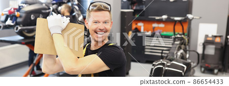Happy male repairman holding clipboard with documents near motorcycle in car repair shop 86654433