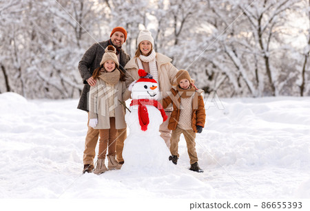 Happy family in warm clothes laughing merrily while making snowman together 86655393