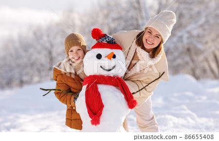 Joyful young mother making snowman with son while playing together in snowy winter park 86655408