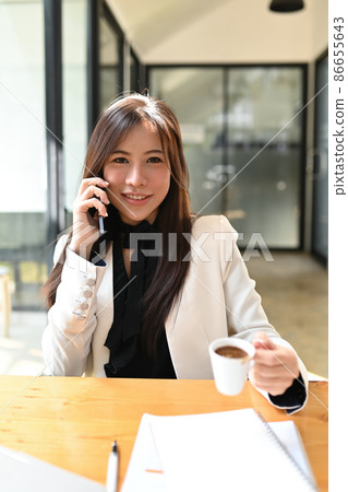 Confident asian businesswoman talking on mobile phone and drinking coffee. Confident asian businesswoman talking on mobile phone and drinking coffee. 86655643