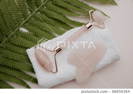 Roller and gua sha massage scraper on a pink background. Selfcare, beauty and health concept. Roller and gua sha massage scraper on a pink background. Selfcare, beauty and health concept. 86656364