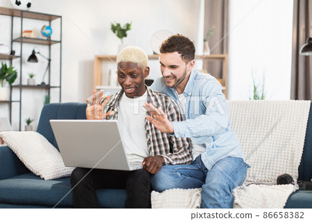 Multi ethnic couple of two gays using laptop for video chat 86658382
